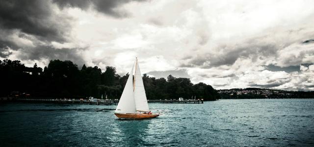 Image of a sailboat sailing on a lake, with cloudy weather above.